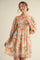woman wearing a short-sleeve peach and blue floral print dress with a tie neck and a loose fit