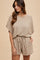 woman wearing a beige textured short-sleeve romper with a cinched waist and side pockets