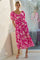 woman wearing a pink floral midi dress with puff sleeves and a tiered skirt, standing by a window
