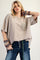 woman wearing a beige oversized t-shirt with crochet pocket and distressed jeans, accessorized with colorful knitted bracelets