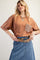 woman wearing a rust-colored oversized t-shirt with a crochet pocket and a denim skirt, smiling at the camera