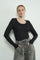 woman wearing a black long sleeve top with a scoop neckline and textured fabric, paired with gray high-waisted pants