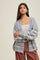 woman wearing a grey striped oversized cardigan with a deep v-neck and light colored stripes paired with a beige top and wide-leg pants