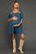 woman wearing a blue maternity dress with puffed sleeves and a drawstring, holding her baby bump and wearing knee-high tan boots
