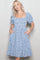 woman wearing a blue and white gingham puff sleeve dress with a smocked bodice and ruffled hem, posing with hands in pockets