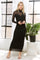 woman wearing a black long sleeve fitted dress with mesh detailing, standing next to a potted plant