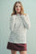 woman wearing a white ribbed long sleeve top with a floral pattern, styled with a burgundy skirt