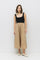 woman wearing a black sleeveless top and a tan midi skirt, standing against a white background