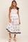 woman wearing a white floral print maternity dress with black trim and shoulder ties, showing off her baby bump