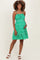 woman wearing a green floral print maternity dress with adjustable straps and tiered ruffle hem, showing her baby bump