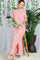 woman wearing a red and white striped maxi dress with short sleeves and a side slit, sitting on a wooden stool