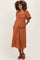 woman wearing a rust-colored maternity dress with puff sleeves and holding her baby bump