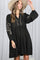 woman wearing a black long sleeve dress with embroidered details and a button front, accessorized with a wide-brimmed hat