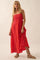 woman wearing a red maxi dress with cut-out details and a flowing silhouette, standing against a neutral background