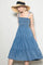 woman wearing a blue denim sundress with spaghetti straps and a tiered skirt, paired with a wide-brim straw hat