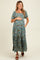 woman wearing a floral maternity maxi dress with short puff sleeves and a baby bump, standing with hands on her belly