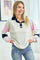 woman wearing a light grey color block pullover with navy and pink sleeves, smiling and posing with hands in pockets