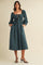woman wearing a teal smocked midi dress with puff sleeves and side pockets, standing on a light background