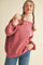 woman wearing a pink off-the-shoulder sweater with a ribbed texture and styled with playful braids