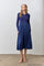 woman wearing a navy ribbed polo sweater and a pleated skirt dress, standing in a minimalist setting