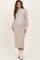 woman wearing a light gray ribbed maternity dress with long sleeves and button details on the cuffs, showing her baby bump