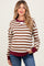 woman wearing a brown and white striped maternity sweatshirt with a burgundy neckline and cuffs, holding her baby bump