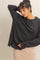 woman wearing a black oversized sweatshirt with dropped shoulders and side slits, paired with a beige skirt