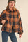 woman wearing a plaid brown and orange cropped jacket with a collar and button details, paired with blue jeans