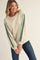 woman wearing a cream sweatshirt with multicolored stripes on the sleeves and paired with dark jeans