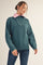 woman wearing a dark teal half-zip sweater with a pink collar and casual jeans