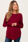 woman wearing a burgundy long sleeve maternity top with a curved hem and holding her baby bump