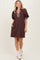 woman wearing a brown puff sleeve dress with a plaid neckline and pockets, standing against a neutral background