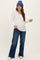 woman wearing a white long sleeve maternity top with buttons and blue wide-leg jeans, showing her baby bump