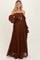 woman wearing a brown lace off-the-shoulder maxi maternity dress, cradling her baby bump
