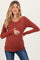 woman wearing a rust colored long sleeve maternity top with button details and holding her baby bump