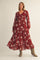woman wearing a red floral maxi dress with long sleeves and a tiered skirt, posing in beige ankle boots