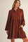 woman wearing a rust-colored long sleeve button-up shirt dress with a flared skirt and pockets