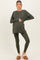 woman wearing a dark green long sleeve maternity top and leggings, holding her baby bump, paired with slippers