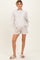 woman wearing a light beige maternity sweatshirt and matching shorts, standing with hands in pockets and wearing slippers
