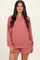 woman wearing a rose-colored oversized sweatshirt and matching shorts, smiling at the camera