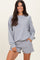 woman wearing a grey long sleeve sweatshirt and matching shorts, smiling at the camera