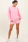 woman wearing a pink oversized sweatshirt and matching shorts, posing against a light background