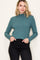 woman wearing a ribbed teal long sleeve top with a scalloped neckline and holding her hands in her pockets
