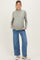 woman wearing a light olive green long sleeve maternity top and blue wide leg jeans, showcasing her baby bump