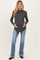 woman wearing a dark gray maternity sweater and blue flared jeans, gently cradling her baby bump