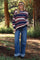 woman wearing a navy and cream striped maternity sweater with dark jeans, standing outdoors among greenery