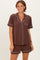 woman wearing a brown short sleeve pajama set with white piping and a pocket