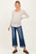 woman wearing a beige long sleeve maternity top and blue wide-leg jeans, showing her baby bump