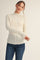 woman wearing a cream long sleeve textured top with a high neckline and fitted sleeves paired with blue jeans