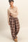 woman wearing a beige zip-up pullover and brown plaid wide-leg pants with buttons, posing in a relaxed manner